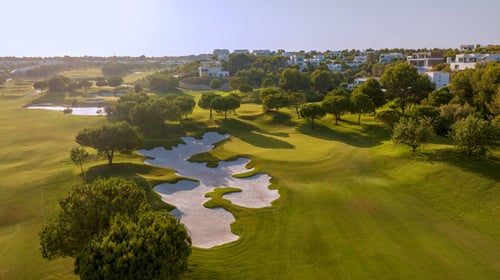 Aerial view of the Las Colinas course in morning light, with a lake, bunkers and villas among the pines