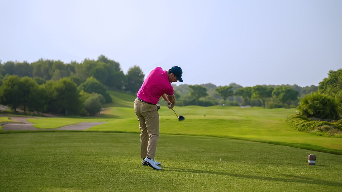 Golfer in a pink shirt mid-swing on a fairway at Las Colinas, framed by pine trees